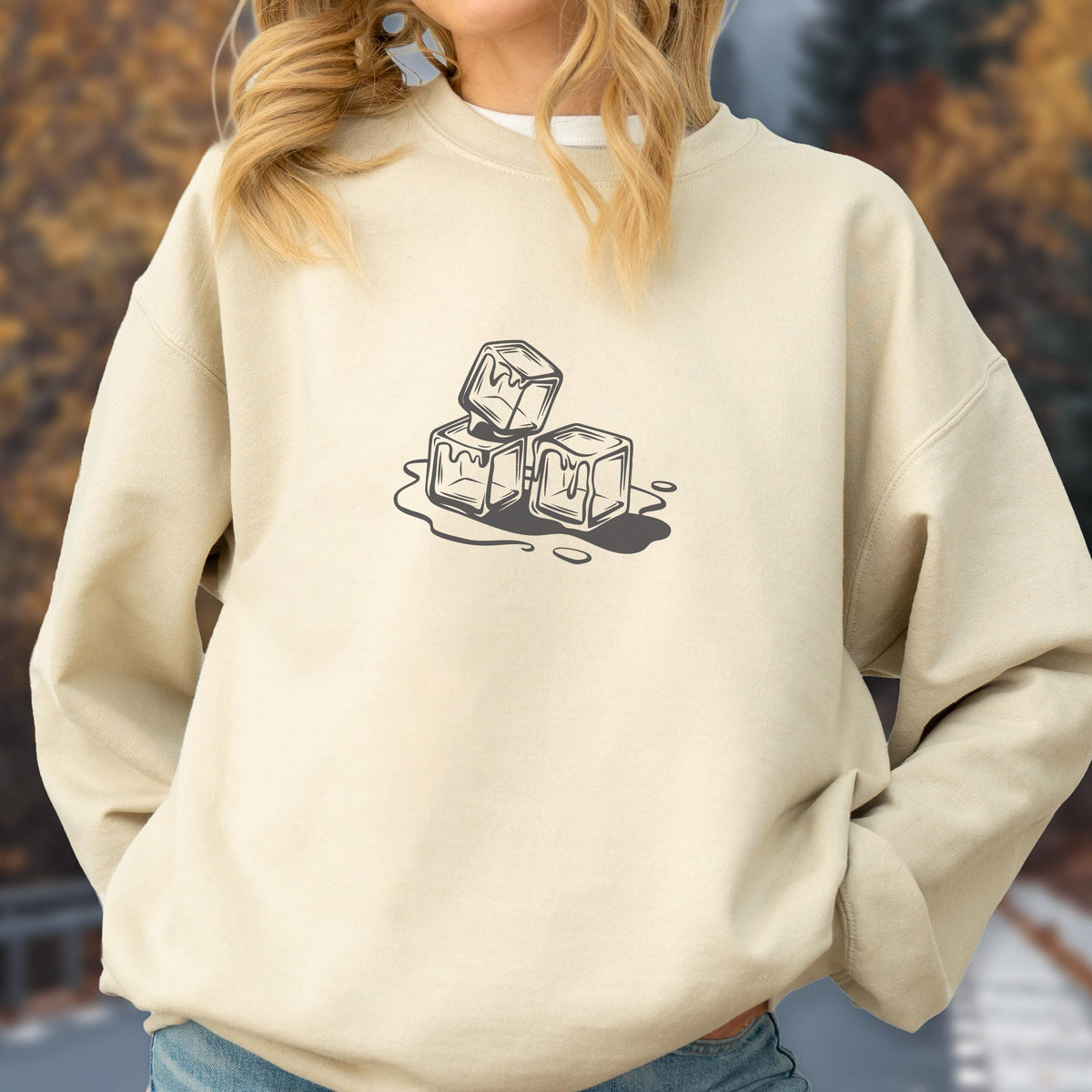 May include: A beige sweatshirt featuring a black and white graphic of three melting ice cubes. The ice cubes are stacked and surrounded by water droplets, creating a cool, refreshing design. The sweatshirt is a casual, comfortable style.