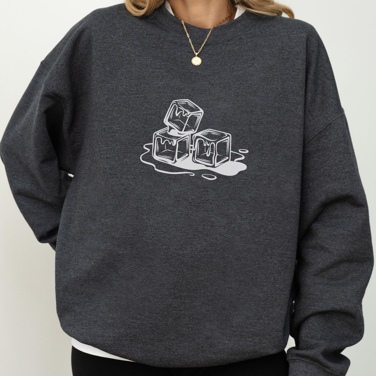 May include: Dark gray sweatshirt featuring a white graphic of three melting ice cubes. The ice cubes are stacked and surrounded by a puddle of water. The sweatshirt is a casual, comfortable style.