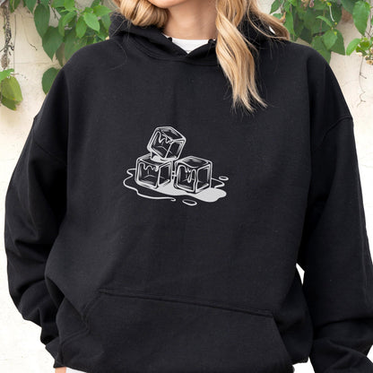 May include: Black hoodie with a white graphic of three melting ice cubes. The design is centered on the chest. The hoodie has a front pocket and a hood. The background is a light-colored wall with green foliage.