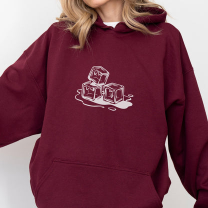 May include: Burgundy hoodie with a white graphic of three melting ice cubes. The design is a simple line drawing, creating a minimalist aesthetic. The hoodie has a drawstring hood and a front pocket.