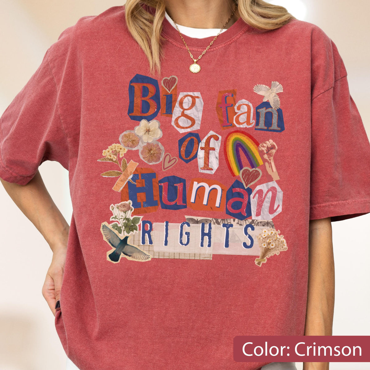 May include: Crimson-colored t-shirt with the text "Big fan of Human Rights" in a collage style. The design includes a rainbow, hearts, flowers, and a bird. The shirt is a relaxed fit.