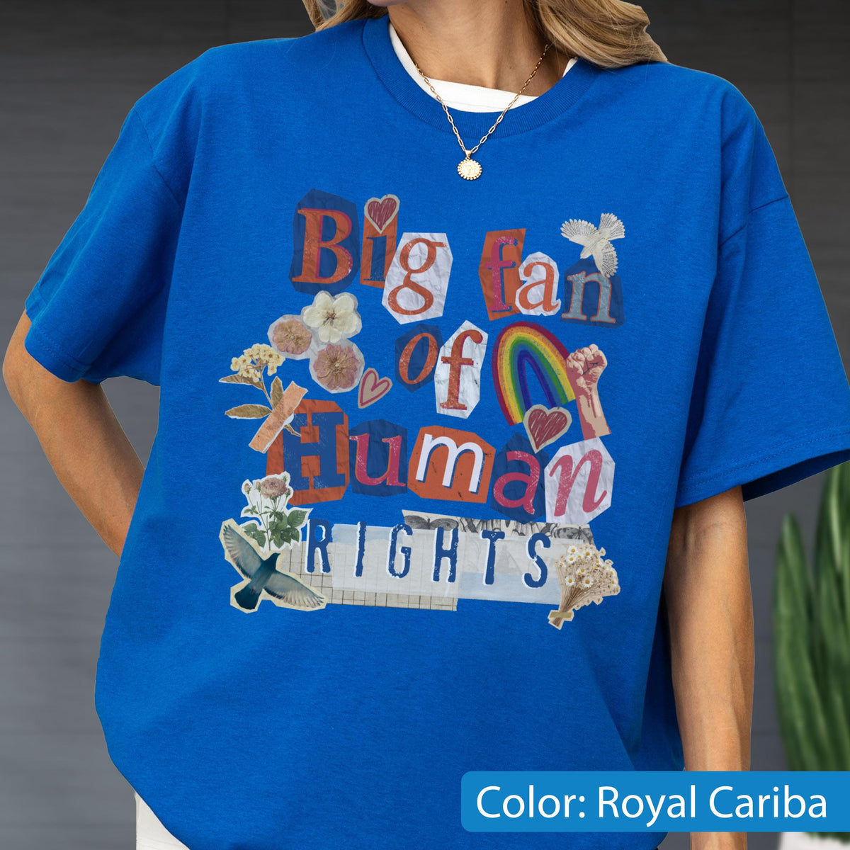 May include: Royal Cariba blue t-shirt with the text "Big fan of human rights" in a collage style. The design includes hearts, a rainbow, flowers, and a dove. The shirt has short sleeves and a crew neck.