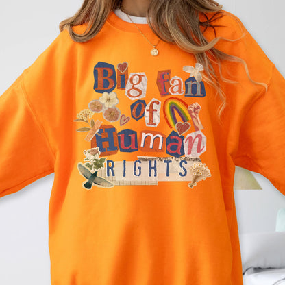 May include: An orange sweatshirt with the text "Big fan of Human Rights" in a collage style. The design includes a rainbow, hearts, and floral elements. The sweatshirt is a solid orange color.