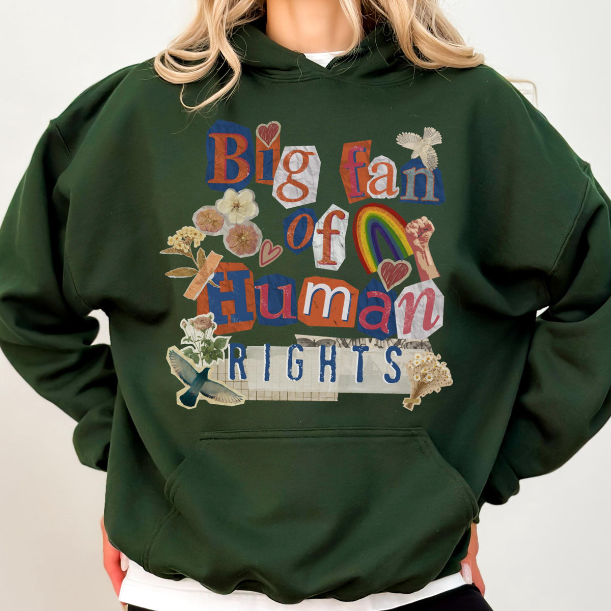 May include: Dark green hoodie with a front graphic that reads "Big fan of Human Rights" in a collage style. The design includes a rainbow, flowers, and a raised fist. The hoodie has a kangaroo pocket and a drawstring hood.