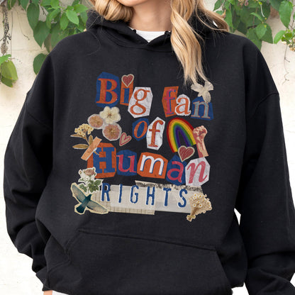May include: Black hooded sweatshirt with the text "Big fan of Human Rights" in a collage style. The design includes a rainbow, flowers, and a raised fist. The sweatshirt is a comfortable, casual style.