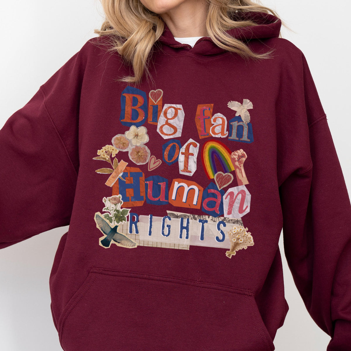 May include: Burgundy hoodie with the text "Big fan of Human Rights" in a collage style. The design includes a rainbow, flowers, and a raised fist. The hoodie is a comfortable, casual garment.