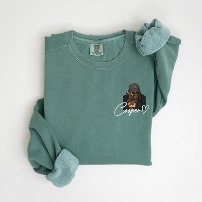 May include: A teal Comfort Colors sweatshirt with a graphic of a dachshund wearing a hat and sunglasses. The name "Cooper" is written in cursive below the graphic, with a heart symbol. The sweatshirt has a crew neck and long sleeves.