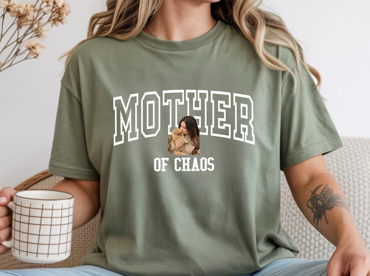 May include: Olive green t-shirt with the words "MOTHER OF CHAOS" in white block letters. A small image of a woman holding a dog is centered below the word "MOTHER".