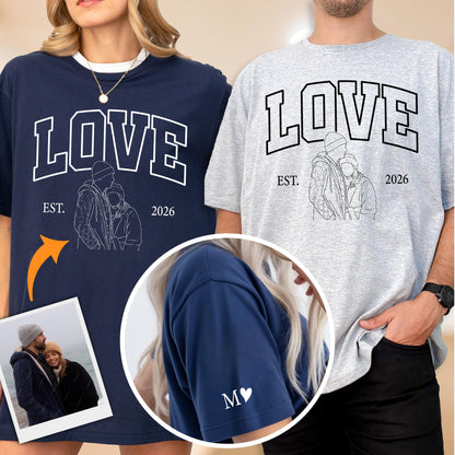 May include: Navy blue and gray oversized t-shirts with the word "LOVE" in white block letters. Each shirt features a line drawing of a couple and the text "EST. 2026". The navy shirt has a white heart and the letter "M" on the sleeve.