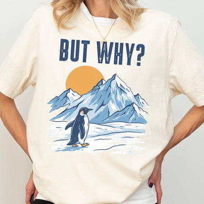 May include: Cream-colored t-shirt featuring a graphic of a penguin standing in front of snow-covered mountains and a yellow sun. The text "BUT WHY?" is printed above the graphic in navy blue.