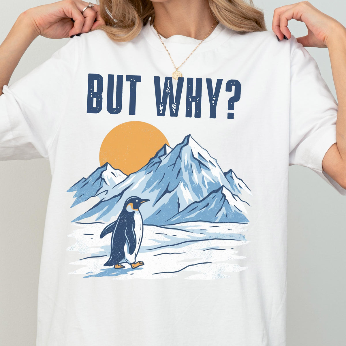 May include: White t-shirt with the text "BUT WHY?" above a graphic of a penguin standing in front of snow-covered mountains and a yellow sun. The penguin is black and white, and the mountains are blue.