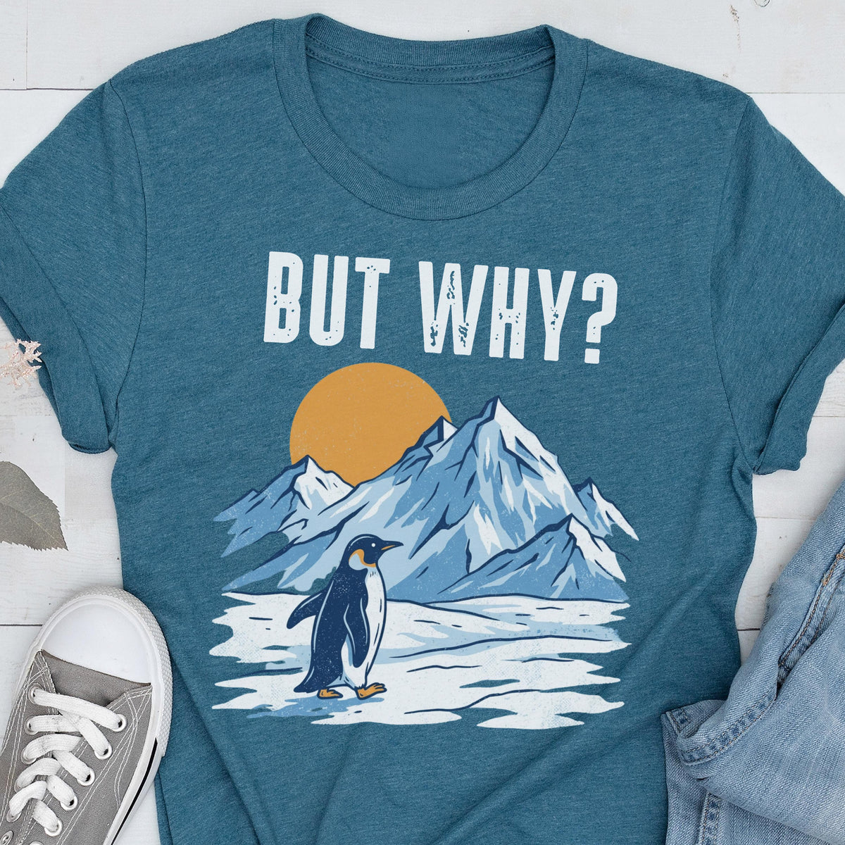 May include: Teal t-shirt with the text "BUT WHY?" above a graphic of a penguin standing on ice in front of mountains and a yellow sun. The penguin is black and white.