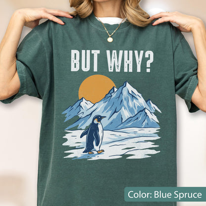 May include: Blue spruce-colored t-shirt with the text "BUT WHY?" above a graphic of a penguin standing in front of snow-covered mountains and a setting sun. The shirt is a solid color.