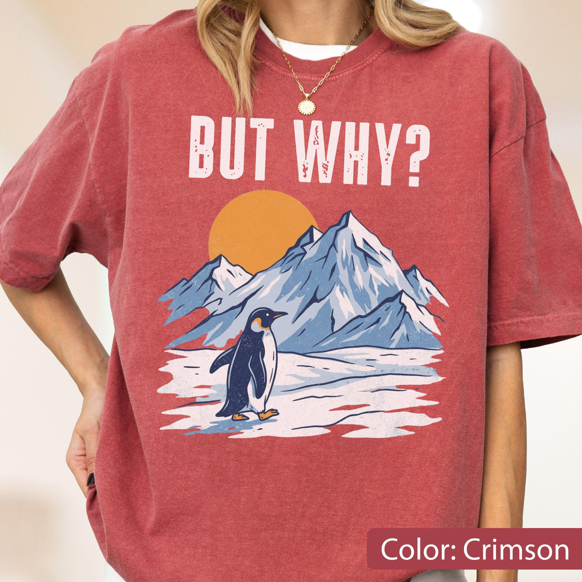 May include: Crimson-colored t-shirt with the text "BUT WHY?" above a graphic of a penguin standing in front of mountains and a setting sun. The shirt's design features a penguin, mountains, and a sun.