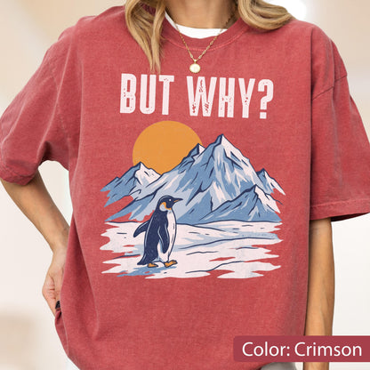 May include: Crimson-colored t-shirt with the text "BUT WHY?" above a graphic of a penguin standing in front of mountains and a setting sun. The shirt's design features a penguin, mountains, and a sun.