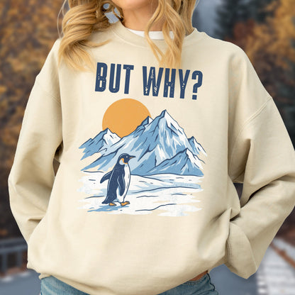 May include: Beige sweatshirt with a graphic of a penguin walking in front of snow-covered mountains and a setting sun. The text "BUT WHY?" is printed above the mountains in navy blue.