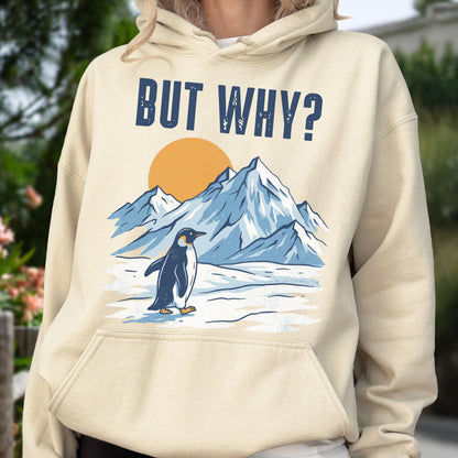 May include: A beige hoodie with a graphic featuring a penguin standing in front of snow-covered mountains and a setting sun. The text "BUT WHY?" is printed above the scene in navy blue block letters. The hoodie has a drawstring hood and a front pocket.