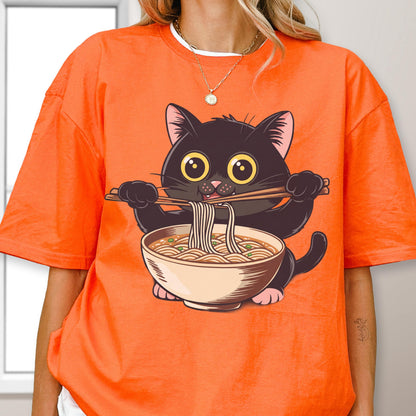 May include: Orange t-shirt featuring a cartoon black cat eating ramen noodles with chopsticks. The cat has large yellow eyes and is holding a bowl of noodles. The shirt is a solid orange color.