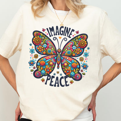 May include: A cream-colored t-shirt featuring a large, colorful butterfly graphic with intricate floral patterns in shades of red, orange, yellow, and blue. The text "IMAGINE" is printed in a dark blue font above the butterfly, and "PEACE" below.