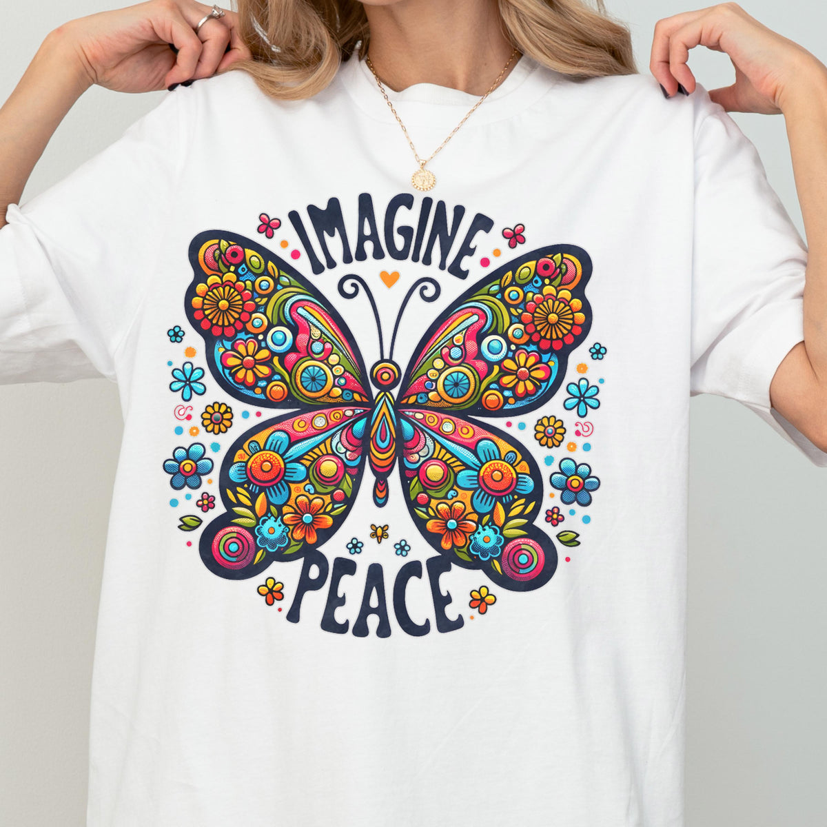May include: A white short-sleeved t-shirt featuring a large, colorful butterfly graphic with intricate floral patterns in shades of red, orange, yellow, and blue. The text "IMAGINE" is arched above the butterfly, and "PEACE" is printed below it.