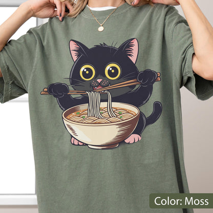 May include: Moss green t-shirt featuring a cartoon black cat eating ramen noodles from a bowl with chopsticks. The cat has large yellow eyes and pink paws. The shirt is a solid color.