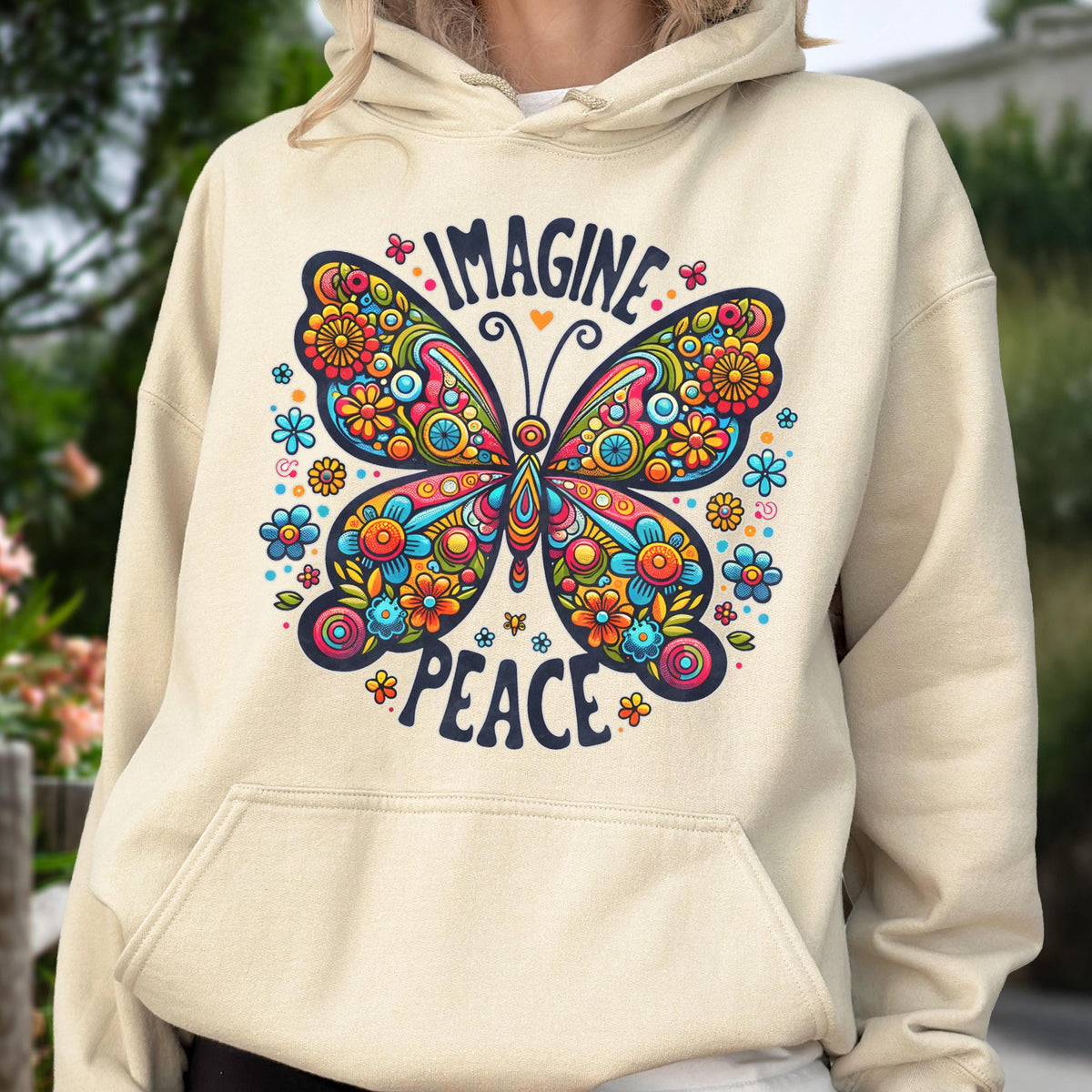 May include: Beige hoodie featuring a colorful butterfly design with the words "IMAGINE" and "PEACE". The butterfly is adorned with flowers in shades of blue, orange, yellow, and pink. The hoodie has a drawstring hood and a kangaroo pocket.
