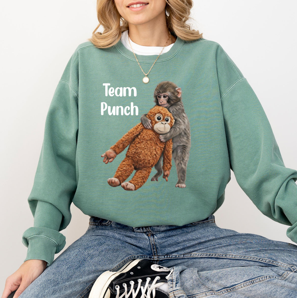 May include: Sage green sweatshirt with the text "Team Punch" and a graphic of two monkeys hugging. One monkey is brown, the other is gray. The sweatshirt has a crew neck and long sleeves.