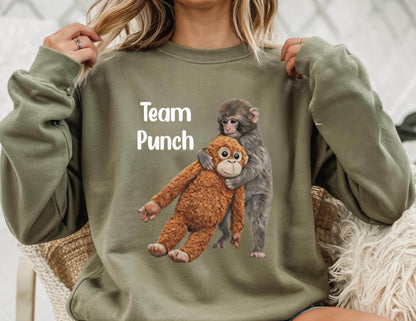 May include: An olive green sweatshirt with the text "Team Punch" in white. The sweatshirt features a graphic of two monkeys hugging. One monkey is brown, and the other is gray.