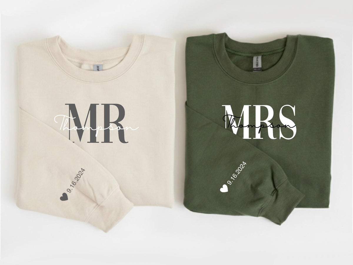 May include: Two crewneck sweatshirts, one beige and one olive green. The beige sweatshirt says "MR Thompson" in dark gray and script font. The olive green sweatshirt says "MRS Thompson" in white. Both sleeves have the date "9.16.2024" and a heart.