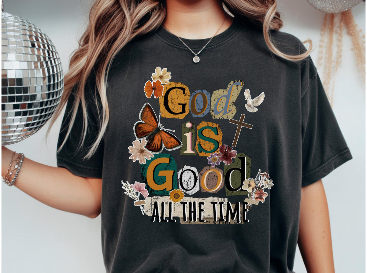 May include: Dark gray t-shirt with the phrase "God is Good All the Time" in a colorful, block letter design. The design includes a butterfly, flowers, a cross, and a dove.