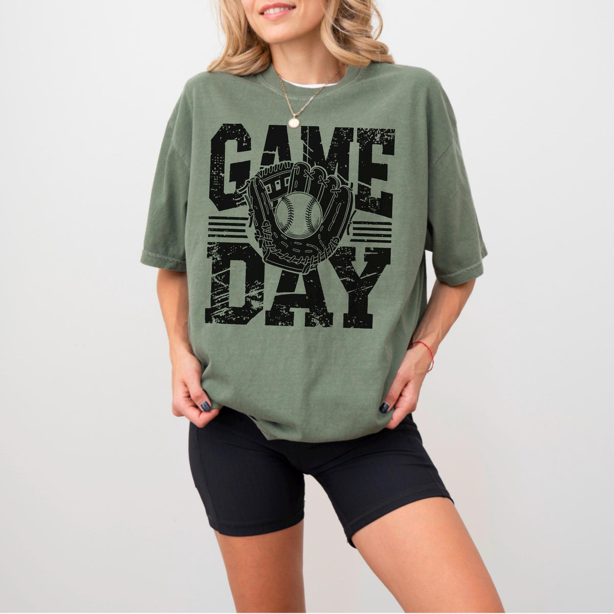 May include: Olive green t-shirt with the words "GAME DAY" in distressed black lettering. A baseball glove and ball graphic is centered between the words. The shirt is a relaxed fit.