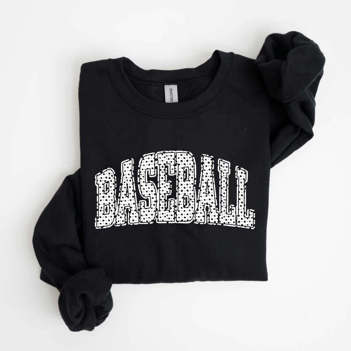 May include: Black sweatshirt with the word "BASEBALL" in large, white, dotted letters across the front. The sweatshirt is folded neatly on a white surface. The sleeves are long and folded.
