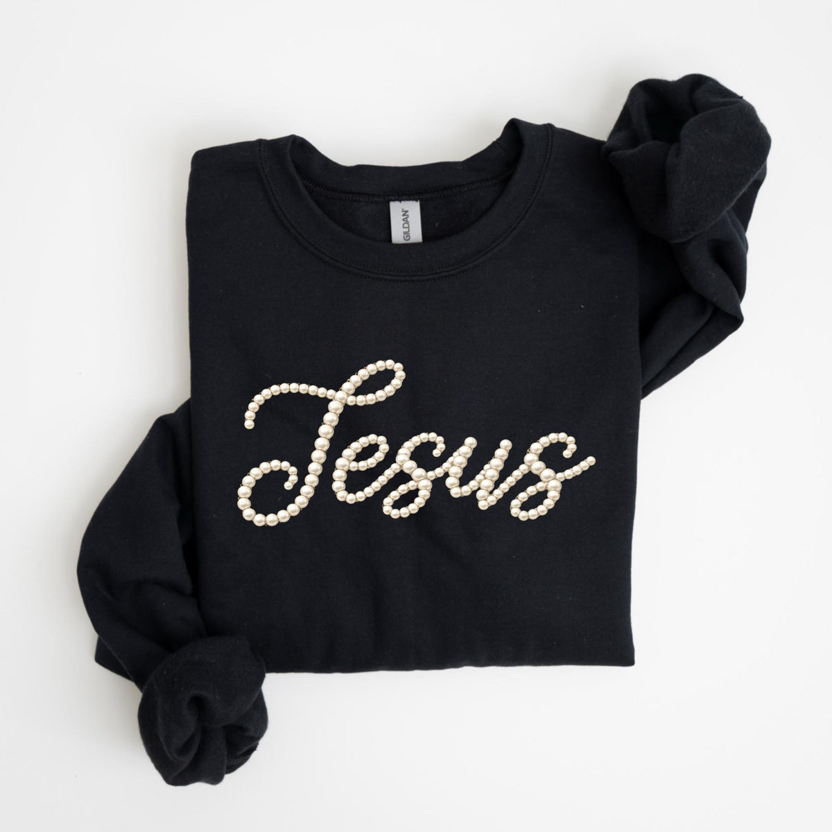 May include: Black sweatshirt with the word "Jesus" spelled out in white pearls. The long-sleeved top is folded neatly, with the sleeves tucked in. The sweatshirt is made of a soft material.