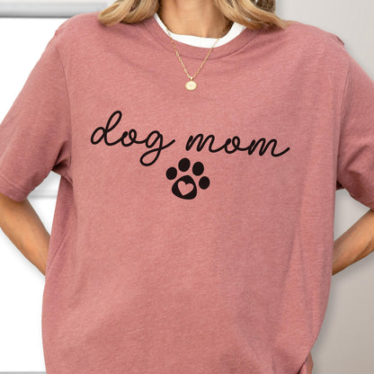 May include: A dusty rose short-sleeved t-shirt with the words "dog mom" in a cursive font, and a paw print with a heart in the center. The shirt has a white crew neck collar.