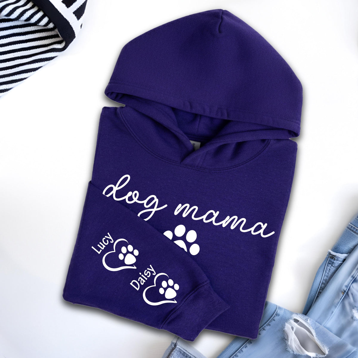 May include: A deep purple hoodie with the words "dog mama" in white script. The sleeve features paw prints and the names "Lucy" and "Daisy". The hoodie has a hood and is folded.