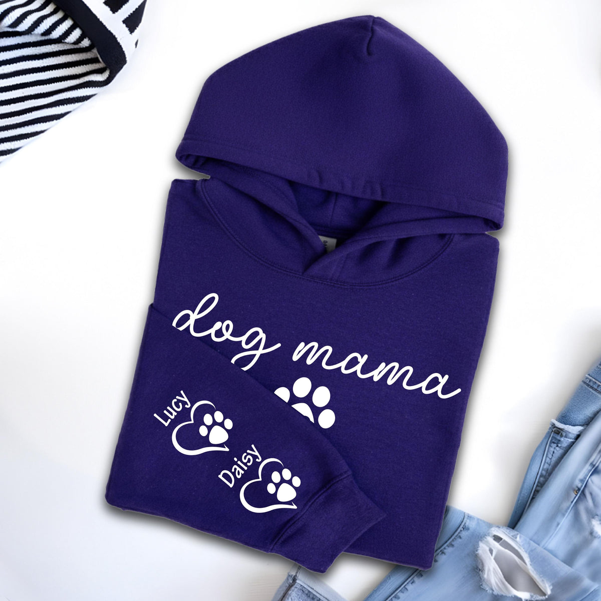 May include: A deep purple hoodie with the words "dog mama" in white script. The sleeve features paw prints and the names "Lucy" and "Daisy". The hoodie has a hood and is folded neatly.