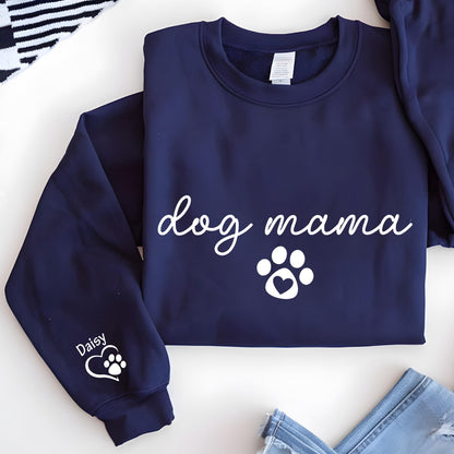 May include: Navy blue sweatshirt with the words "dog mama" in white script, along with a paw print design. The left sleeve has the name "Daisy" and a paw print. The sweatshirt is folded, with a portion of a pair of jeans visible.