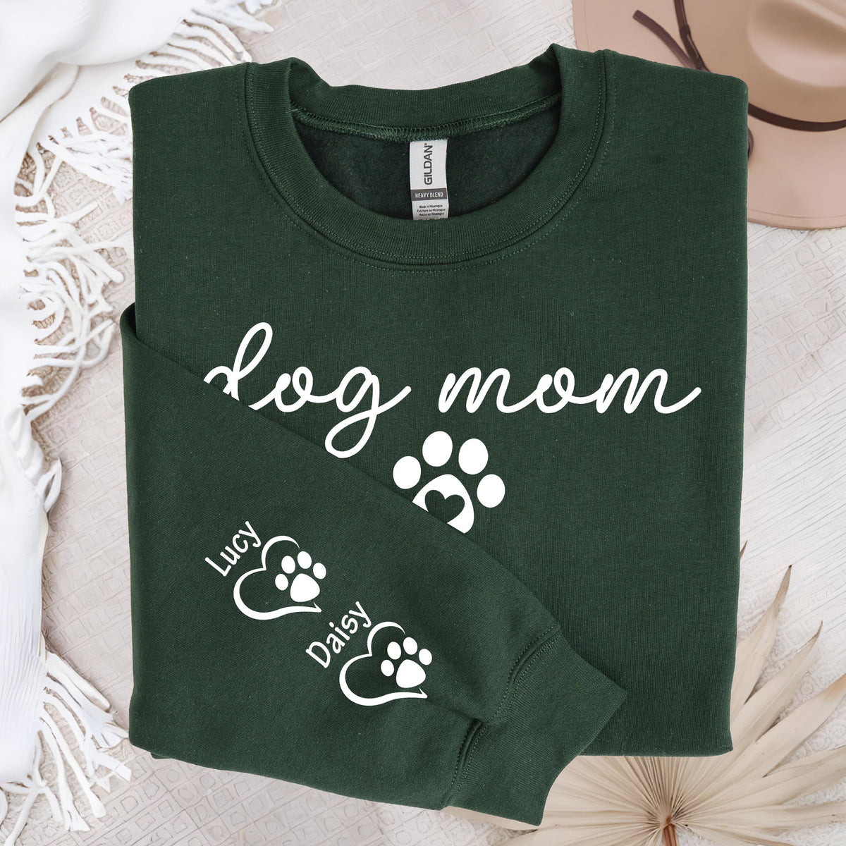 May include: Dark green sweatshirt with the words "dog mom" in a cursive font, along with paw print graphics. The sleeve features the names "Lucy" and "Daisy" with paw prints inside hearts. A cozy apparel item.
