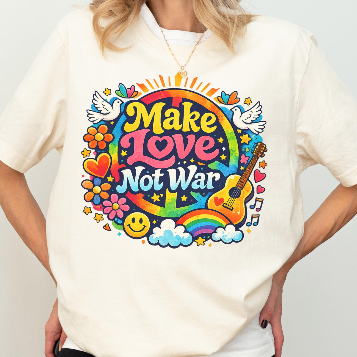 May include: Cream-colored t-shirt featuring a colorful graphic with the words "Make Love Not War." The design includes a peace sign, rainbow, guitar, flowers, doves, and a smiley face. The shirt has short sleeves and a crew neck.