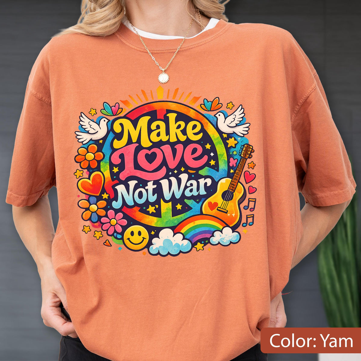 May include: A yam-colored t-shirt with a colorful graphic that says "Make Love Not War." The design includes a peace sign, rainbow, guitar, flowers, doves, and a smiley face. The shirt is short-sleeved.