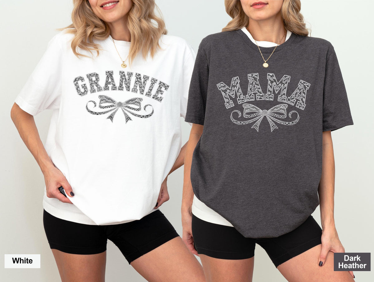 May include: Two women wearing white and dark heather gray t-shirts. The white shirt says "GRANNIE" in a decorative font above a bow design. The dark heather gray shirt says "MAMA" in a decorative font above a bow design. Both shirts have short sleeves.