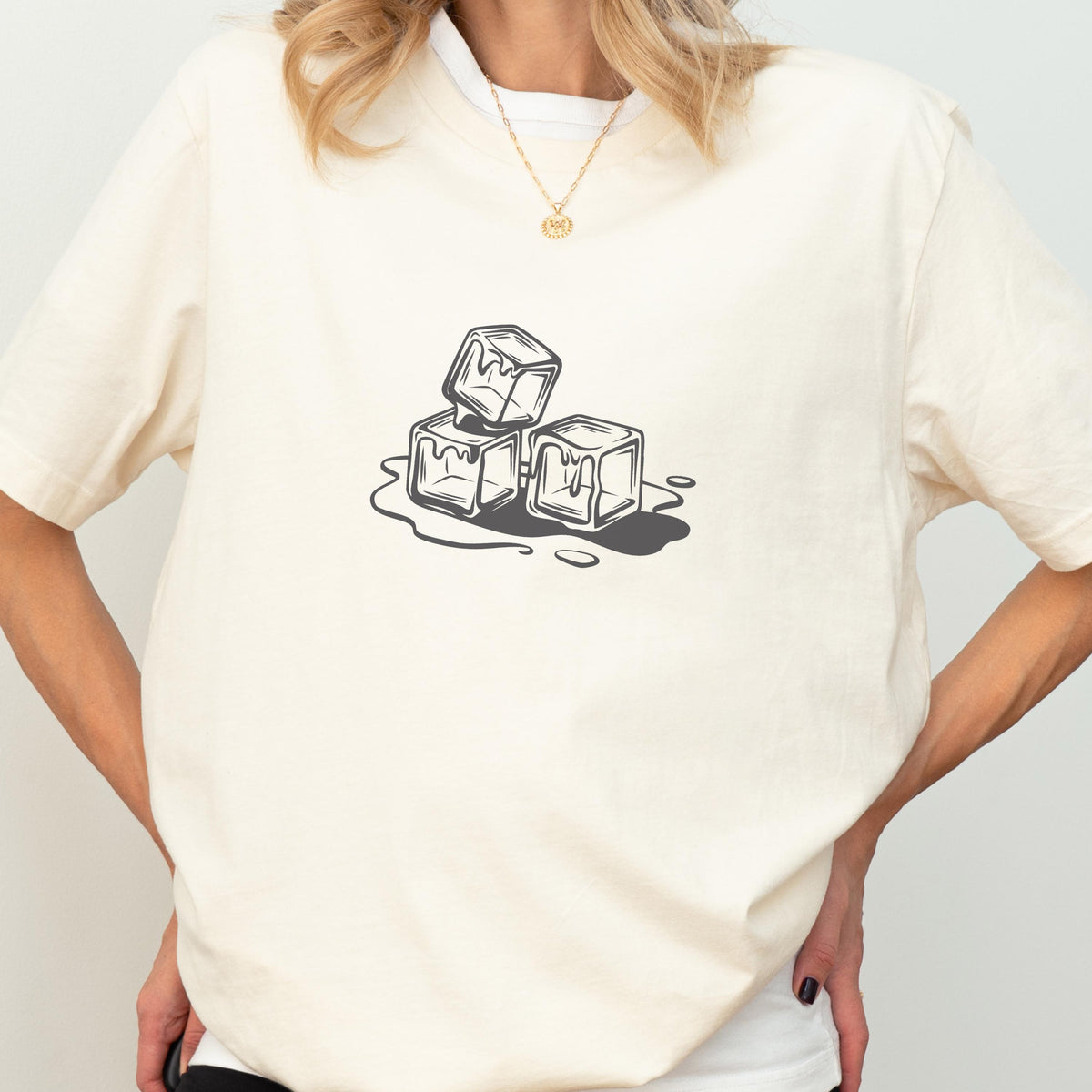 May include: Cream-colored t-shirt featuring a black and white graphic of three melting ice cubes. The design is centered on the front of the shirt. The shirt has short sleeves and a crew neck.