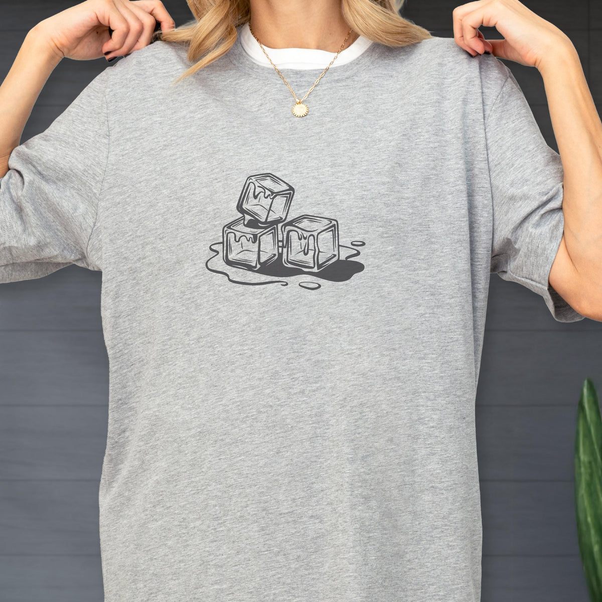 May include: A light gray t-shirt featuring a graphic of three melting ice cubes. The ice cubes are depicted in a simple, black and white line drawing style, with water droplets around them. The shirt has a crew neck and short sleeves.