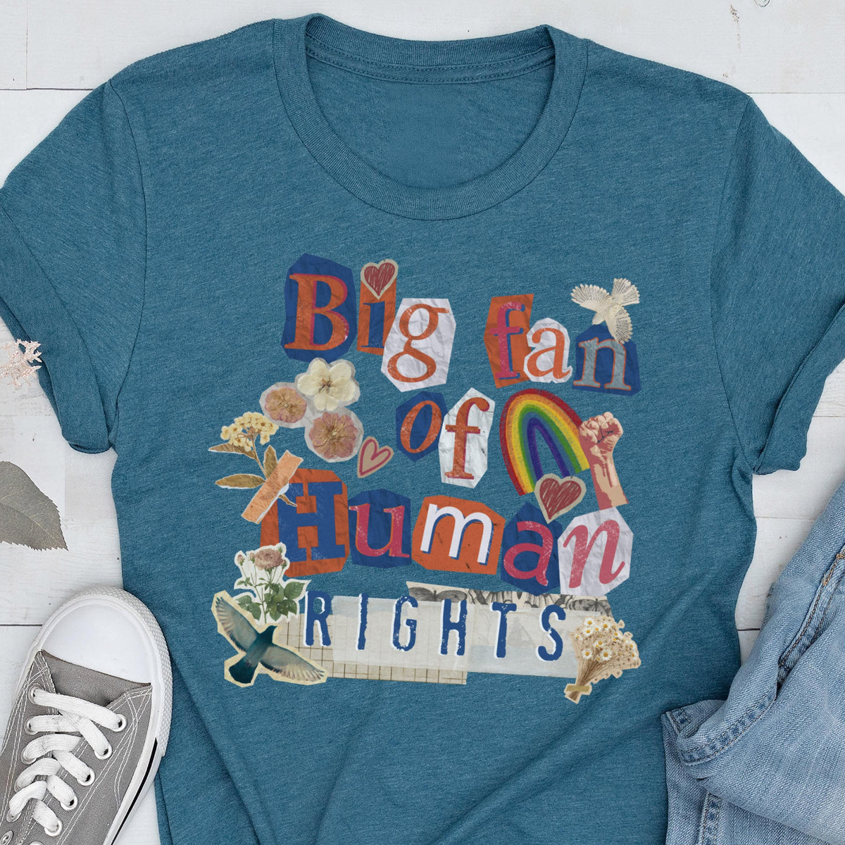 May include: Teal t-shirt with a collage design that reads "Big fan of Human Rights." The design includes a rainbow, hearts, flowers, and a raised fist. The shirt is made of a soft material.