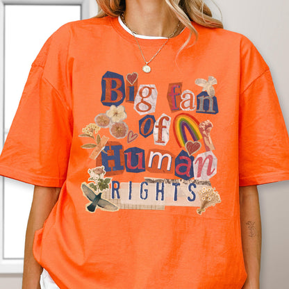 May include: An orange t-shirt with the text "Big fan of Human Rights" in a collage style. The design includes a rainbow, flowers, and a bird. The shirt has a crew neck and short sleeves.