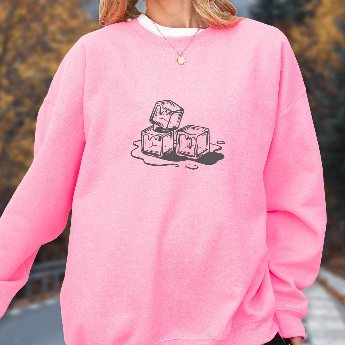 May include: A bright pink sweatshirt featuring a graphic of three melting ice cubes in a black and white line drawing. The ice cubes are positioned on a puddle of water, creating a cool, refreshing design.