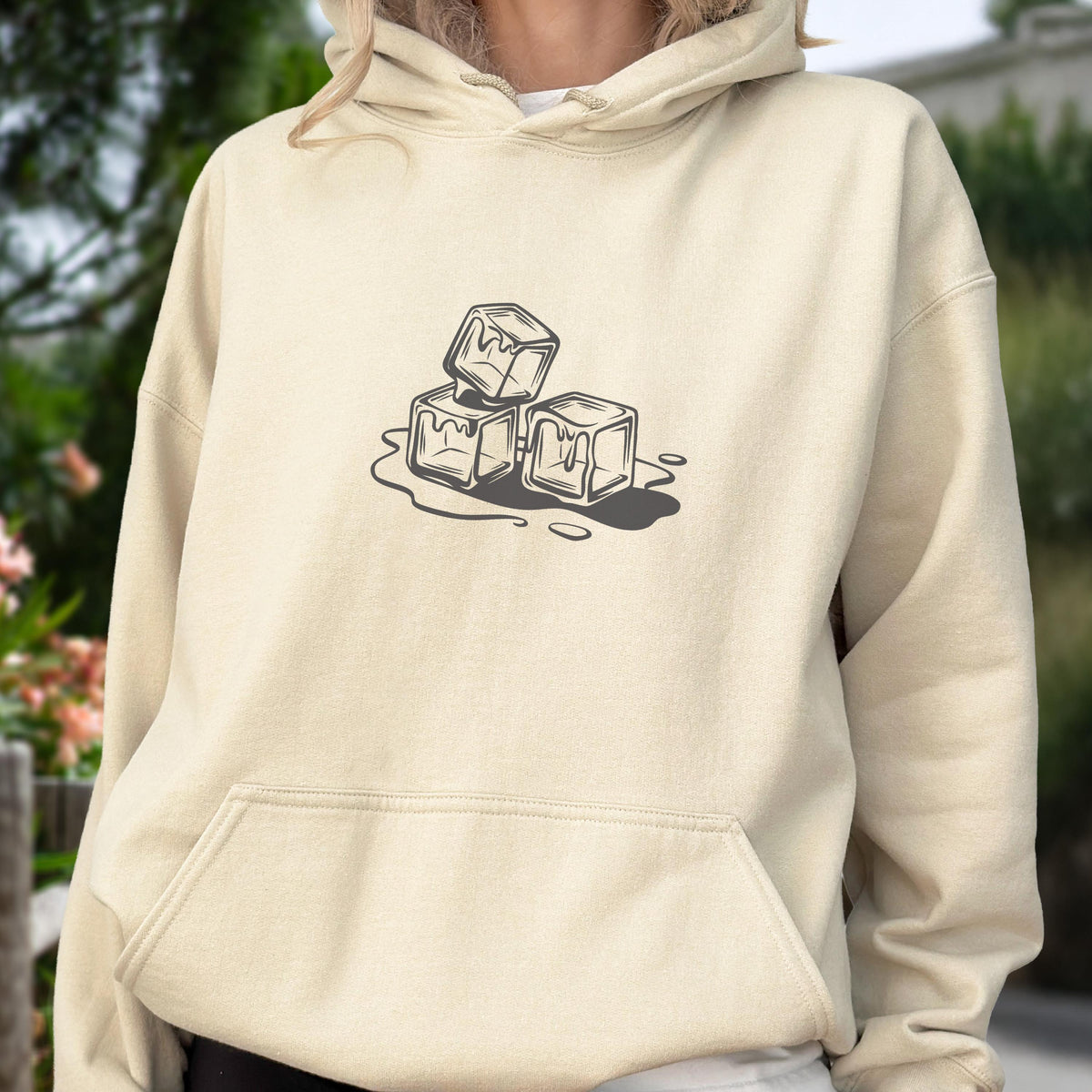 May include: A beige hoodie with a front pocket and a drawstring hood. The hoodie features a graphic of three melting ice cubes in a dark gray color. The ice cubes are stacked on top of each other, with water droplets around them.