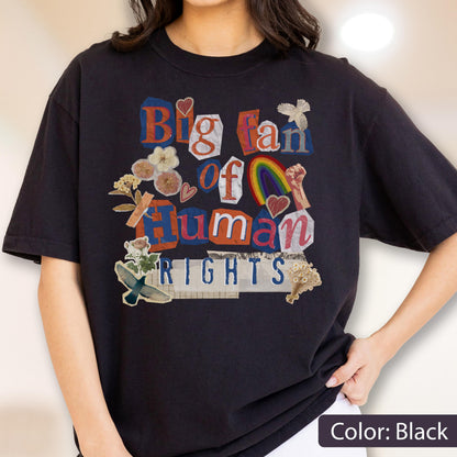 May include: Black t-shirt with a colorful collage design. The design includes the text "Big fan of Human Rights" in a mix of fonts and colors, along with images of a rainbow, flowers, and a raised fist. The shirt is a casual, unisex style.