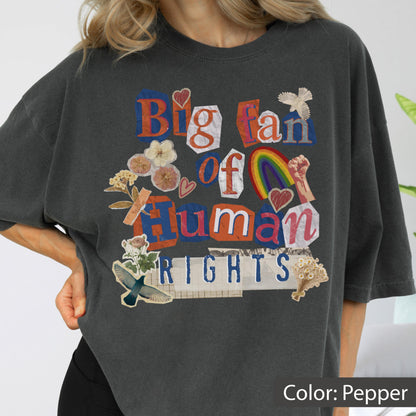 May include: Pepper-colored t-shirt with a collage design. The design includes the words "Big fan of Human Rights" in a mix of fonts and colors, along with images of a rainbow, hearts, and flowers.