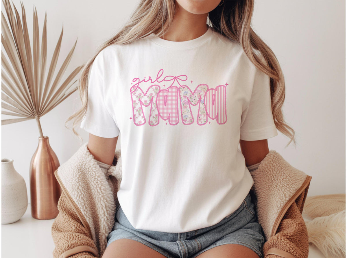 May include: White t-shirt with the text "girl Mama" in pink. The word "Mama" is designed with floral, gingham, and striped patterns. A pink bow is above the word "girl".